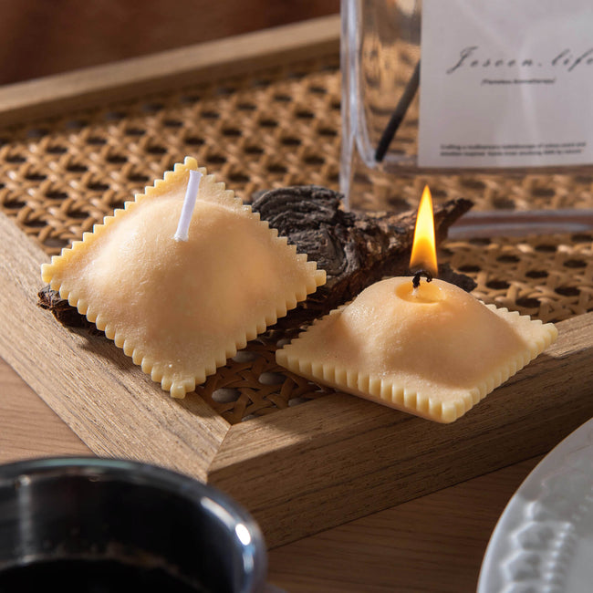 Realistic Ravioli Food Pasta Candle set, and one of them is lit up and sitting on the plate as a unique candle gift. 